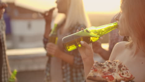 A-women-eat-piece-of-hot-pizza-and-drink-beer-from-a-green-glass-bottle-on-the-party-with-his-fried-in-hot-summer-day.